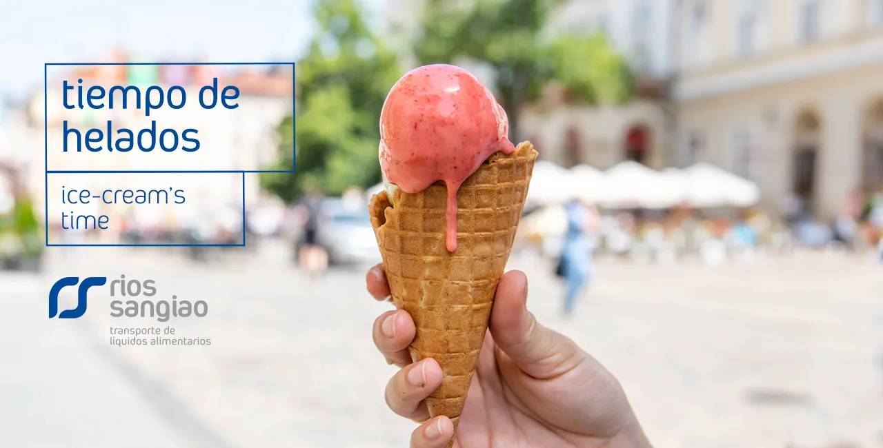 Mano sosteniendo un cucurucho de helado de fresa con una plaza al fondo.
